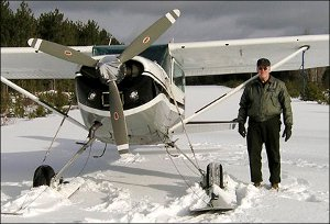 Warden Service Pilot Daryl Gordon is seen standing next to his plane on a frozen lake.