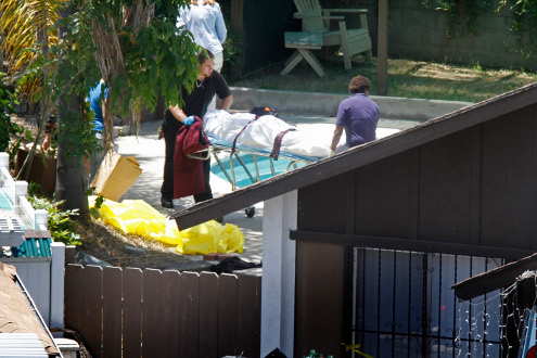 Medical examiners move the body of an adult found dead with three other family members.