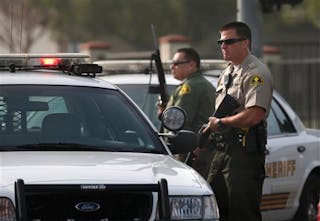 Two San Bernardino County deputies stand guard near the area where a shooting took place in Riverside, Calif. on Feb. 7.
