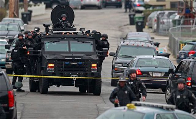 Police in tactical gear arrive on an armored police vehicle as they surround an apartment building while looking for a suspect in the Boston Marathon bombings in Watertown, Mass. on April 19.
