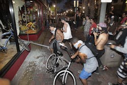 Rioters celebrate, loot and steal a bike after smashing a stop sign through the windows of Easyrider business on the corner of Main and Orange Streets downtown Main Street in Huntington Beach, Calif. on July 28.