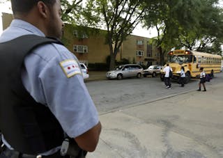 A Chicago Police officer patrolling the neighborhood watches school children board a buss outside Gresham Elementary School on the first day of classes on Aug. 26.