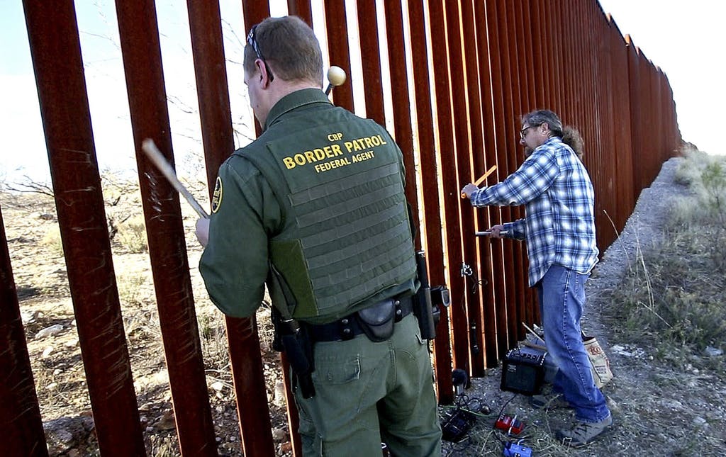 A Border Patrol agent, left, joins Glenn Weyant for a duet, as they bang mallets against the border fence in Sasabe, Ariz., turning it into a musical instrument on Jan. 25.