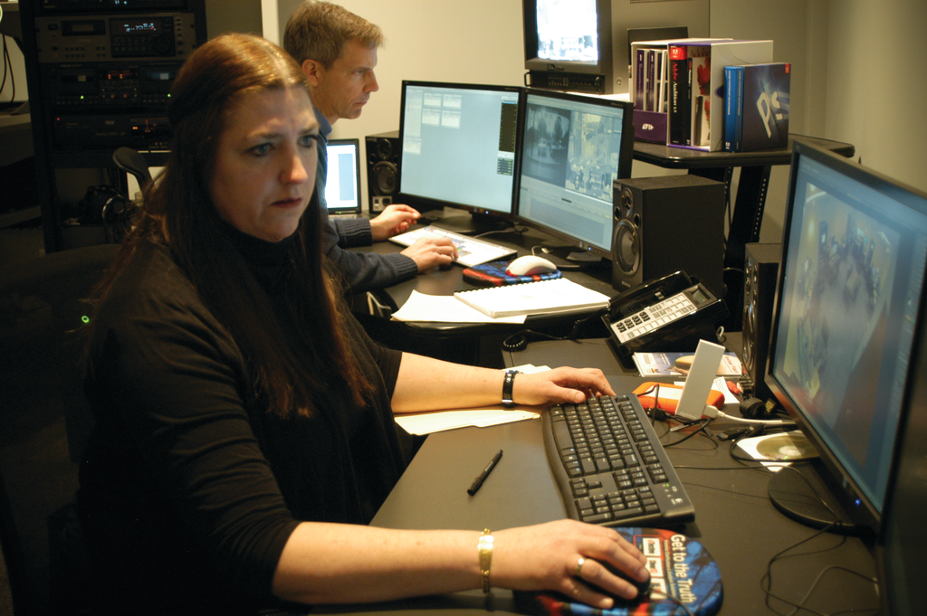 Cathy Eckhardt is seen working, with Paul Munson in the background, inside the New York State Police Forensic Video and Multimedia Services unit's newly renovated office.