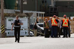 Mill workers talk as a police officer walks away following a shooting at Western Forest Products in Nanaimo, British Columbia on April 30.