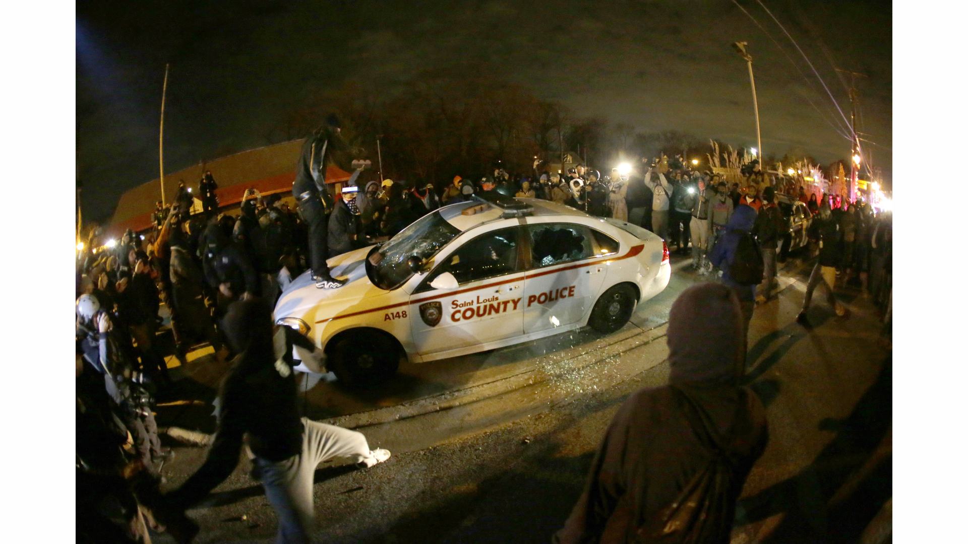 A protester squirts lighter fluid on a police car as the car windows are shuttered near the Ferguson Police Department on Nov. 24.