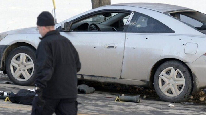 An investigator walks by a car that was pockmarked with bullet holes during a shootout Sunday in Canaan, Maine.