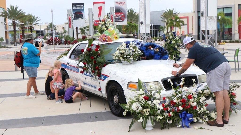 Visitors take the time to sign Daytona Beach, FL, Police Officer Jason Raynor's patrol car in Victory Circle at One Daytona on Friday.