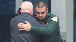 Former Daytona Beach, FL, Police Chief Craig Capri hugs a sheriff's deputy outside the News Journal Center on Sunday during the viewing for slain Officer Jason Raynor.