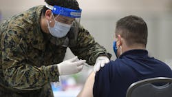 A member of the U.S. military administers a COVID-19 vaccine to a police officer at a FEMA community vaccination center in March in Philadelphia.