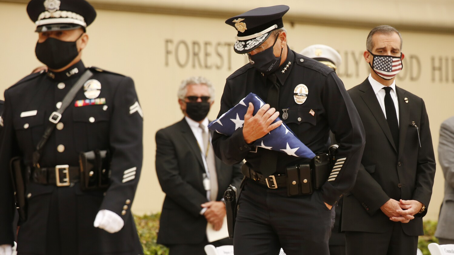 LAPD Chief Michel R. Moore carries the U.S. flag in August 2020 to present to Megan Flynn, the pregnant domestic partner of Officer Valentin Martinez, who was the department's first sworn employee to die of complications from the COVID-19.