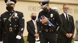 LAPD Chief Michel R. Moore carries the U.S. flag in August 2020 to present to Megan Flynn, the pregnant domestic partner of Officer Valentin Martinez, who was the department's first sworn employee to die of complications from the COVID-19.