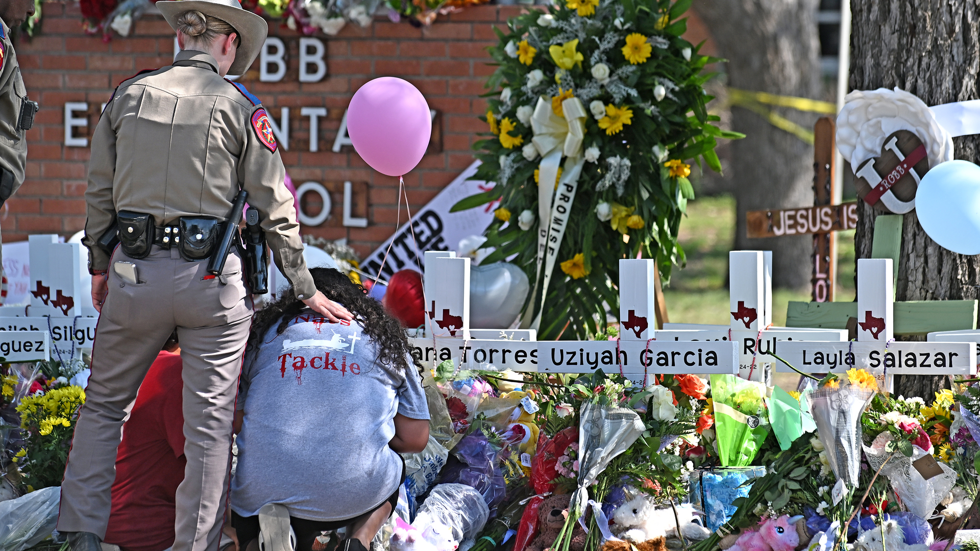 A police officer comforts family members at a memorial outside Rob Elementary School in Uvalde, TX, on Thursday. Nineteen students and two teachers died when a gunman opened fire in a classroom Tuesday.