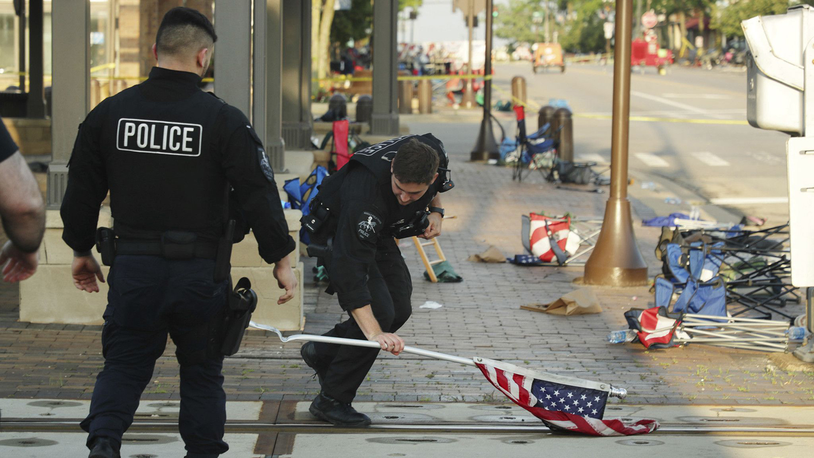 A police officer picks up a water-logged American flag Tuesday, left behind after the mass shooting during a Fourth of July parade in Highland Park, IL.