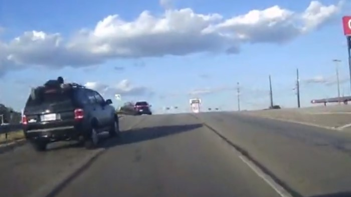 The owner of a stolen SUV hangs on to the vehicle's roof rails as an alleged thief speeds through traffic during a high-speed chase with Live Oak, TX, police Tuesday.
