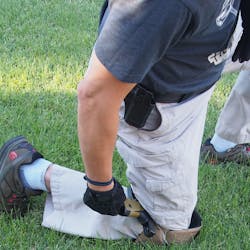 In order to do a one-handed magazine change, the gun needs to somehow be pinned in a stable location. This is one method where it is pinned behind the knee in a kneeling position. Some shooters are very competent with simply stuffing the firearm into the belt, changing magazines, and releasing the slide by using the slide stop, or the belt. Whatever method is used should be practiced regularly.