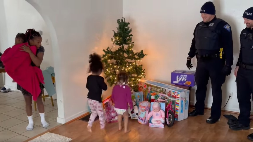South Bend, IN, police officers watch as a family reacts to finding replacement gifts Christmas Eve after the home was robbed earlier, and the holiday presents stolen.