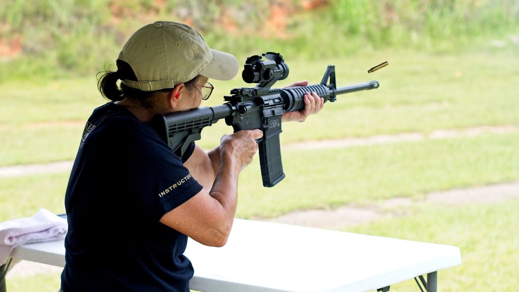A woman fires an AR-15 rifle at a shooting range.