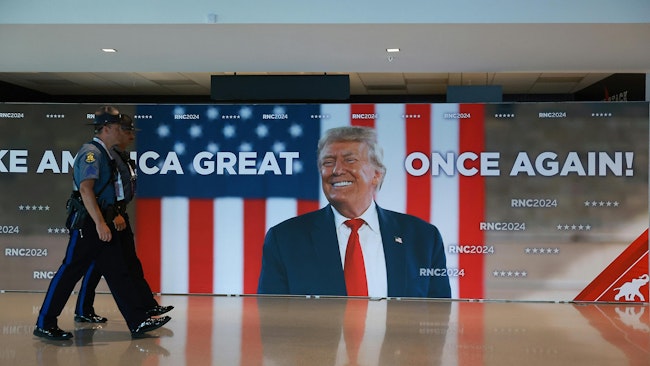 Law enforcement officers walk past a Donald Trump sign in the Fiserv Forum as preparations are underway for the Republican National Convention on Sunday, July 14, 2024, in Milwaukee, Wisconsin. The RNC will be held in Milwaukee from July 15-18.