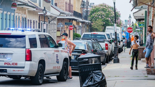 A handcuffed suspect stands next to a Louisiana State Police cruiser as bystanders look on in New Orleans' French Quarter in 2020.