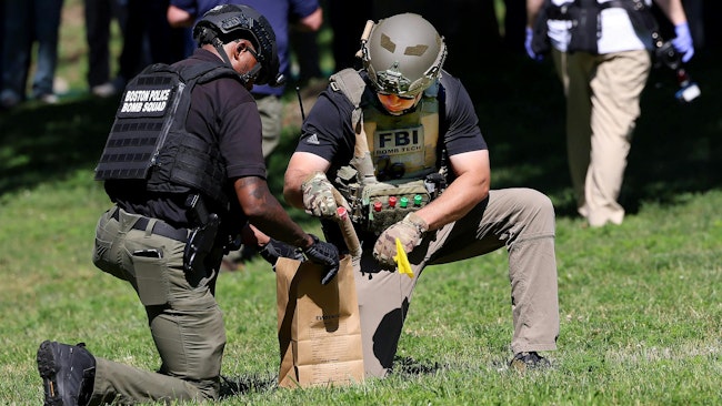 A Boston Police bomb squad technician, left, and an FBI bomb tech collect evidence on Boston Common across from the State House, where the front steps and gate were spray-painted with graffiti overnight Wednesday.