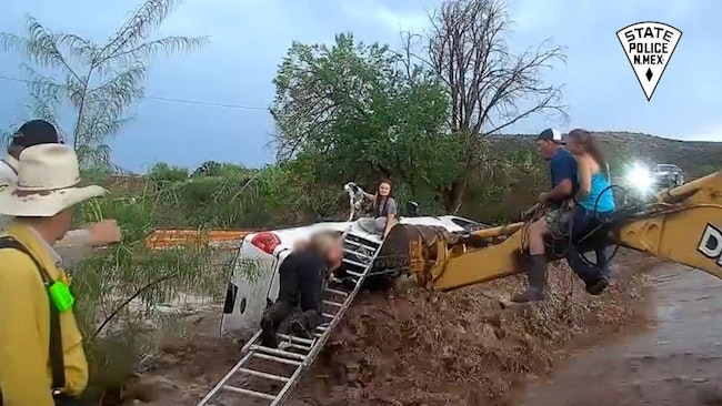 A New Mexico State Police officer used a backhoe and ladder to rescue a woman, her child and their dog after they were trapped when rushing muddy water flipped over their car.