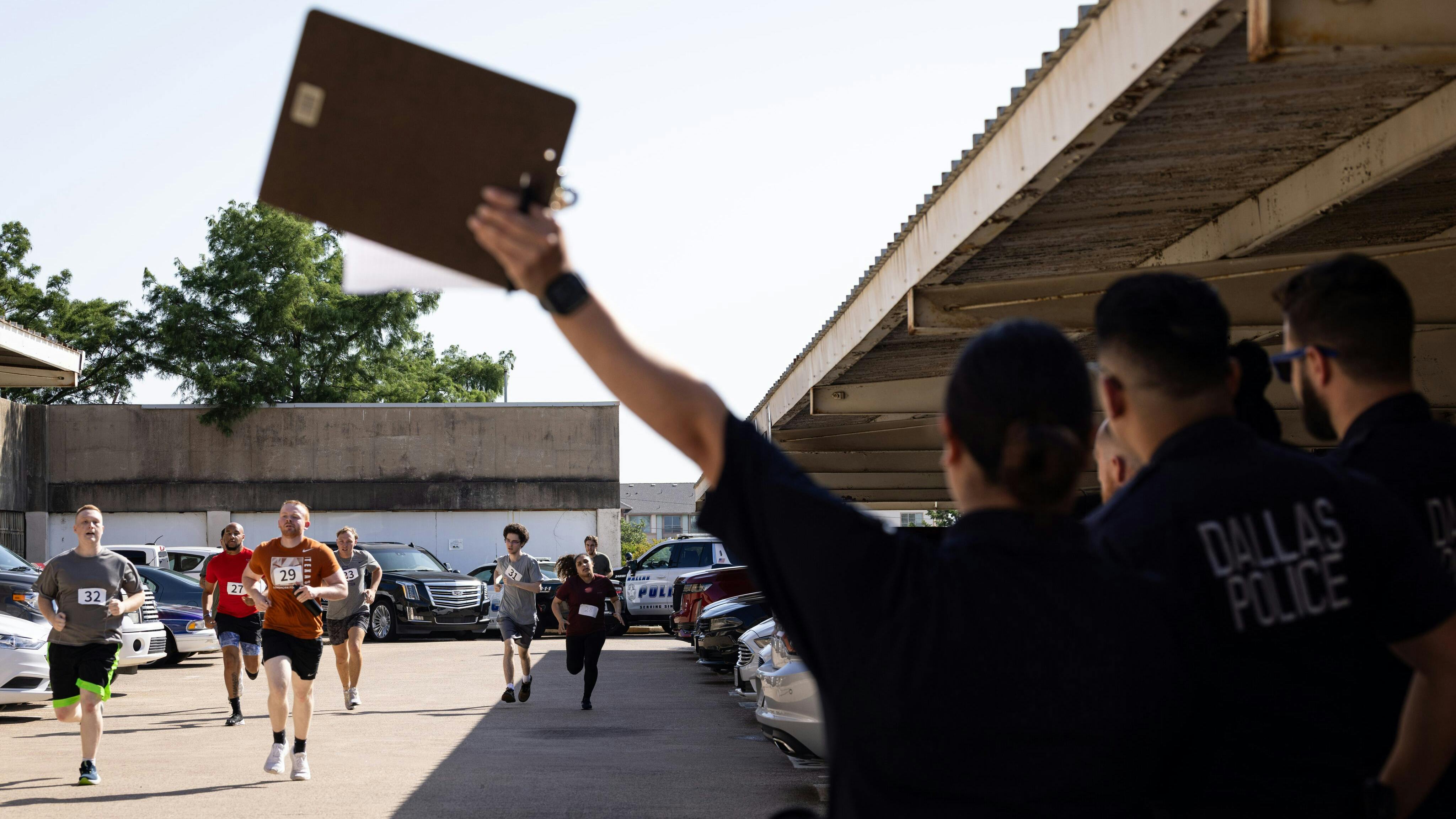 Dallas Police Officer Alyssa Flores calls out times for applicants running a 300-meter run during a July recruitment event at police headquarters.