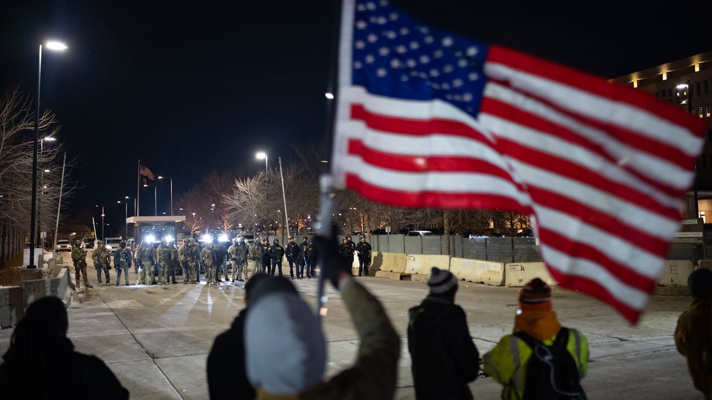 Demonstrators wave flags and chant from across the street while federal agents stand in front of an entrance to the Whipple Federal Building at Fort Snelling on Jan. 11.