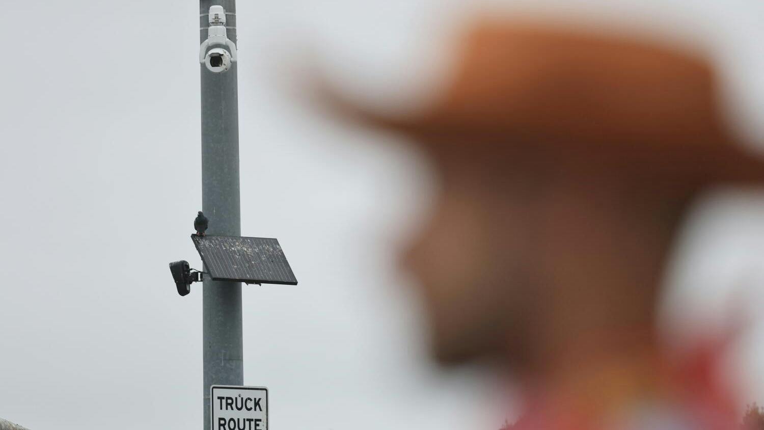 A pedestrian waits to cross the street as a Flock Safety camera is mounted high on traffic signal pole at the intersection of Chapman Avenue &amp; Harbor Boulevard in Garden Grove on Friday, Aug. 14, 2026.
