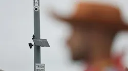 A pedestrian waits to cross the street as a Flock Safety camera is mounted high on traffic signal pole at the intersection of Chapman Avenue & Harbor Boulevard in Garden Grove on Friday, Aug. 14, 2026.