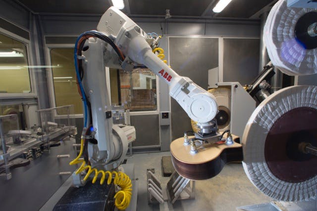 An ABB IRB 4600 robot positions a guitar body against the buffing wheel.